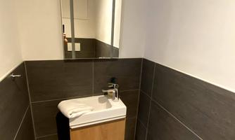 A modern small bathroom with an elegant sink and a large mirror. The walls are tiled in dark colors, creating a stylish contrast.