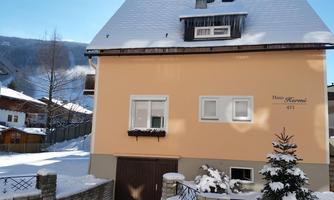 A pretty house in the snow with a bright facade. The garden is covered in snow and surrounded by trees in a winter landscape.