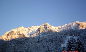 A picturesque mountain panorama with snow-covered peaks. The clear sky radiates in warm colors.