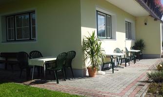 A cozy outdoor area with tables and chairs. The sun is shining on the terrace and there are some plants.