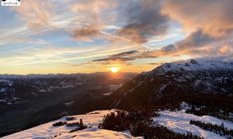 An impressive sunset over snow-covered mountains. The landscape is characterized by gentle hills and a clear sky.
