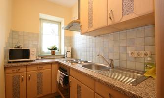 A modern kitchen with light wooden cabinets and a sink. It is well equipped with a microwave and a stove.