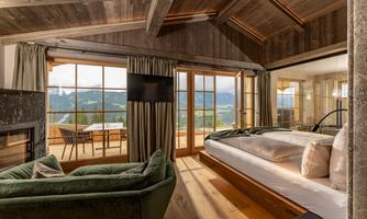 A stylish room with wooden furniture and panoramic windows that offer a wonderful view of the mountains. The room is furnished with a large bed and a cozy seating area.
