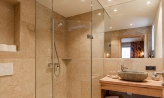 A modern bathroom with a glass shower and elegant stone walls. The wooden vanity is decorated with towels and accessories.