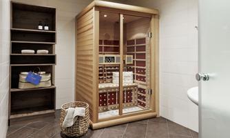 A modern infrared cabin made of wood with a glass front in an elegant room. Next to it is a shelf with care products and towels.