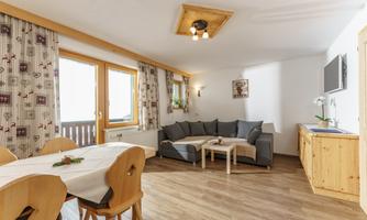 A cozy living area with an L-shaped couch and a dining table. Large windows let in plenty of light and offer a view outside.