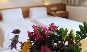 A cozy hotel room with two beds and soft light sources. A bouquet of colorful flowers sits on the table.