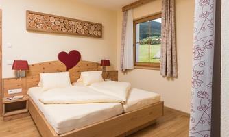 A cozy bedroom with a large wooden double bed featuring a heart-shaped headboard. The windows offer a view of the green landscape outside.