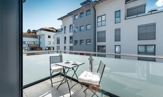 A sunny balcony with a small table and two chairs. In the background, modern buildings are visible.