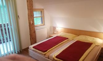 A cozy bedroom with two beds and red blankets. Large windows provide plenty of daylight.