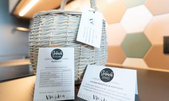 A braided basket with labels and information cards is on a work surface. The background has colorful hexagonal tiles.