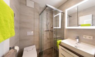 A modern bathroom with a walk-in shower and an elegant sink. Bright green towels complement the simple, bright design.
