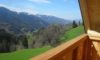 A view from a balcony overlooking green hills and mountain landscapes. The sky is clear with a few clouds.
