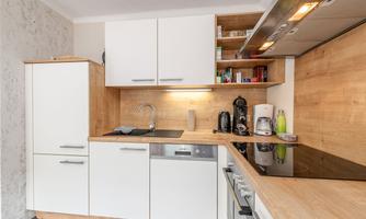 Modern kitchen with white cabinets and wooden shelves. Well equipped with appliances like coffee maker and stove.