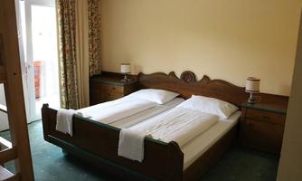 A cozy bedroom with two single beds and bright curtains. There are bedside tables and access to a balcony.