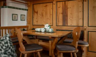A cozy dining area with a wooden table and chairs. On the table is a teapot with cups, surrounded by wood paneling.