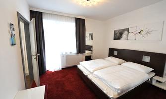 A modern bedroom with a double bed and a red carpet.  
Large windows let in plenty of light and the walls are decorated.