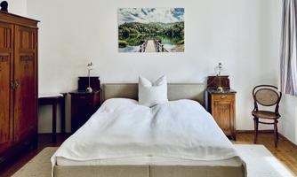 A cozy bedroom with a large bed and an artistic wall mural. Antique furniture gives the room a warm atmosphere.
