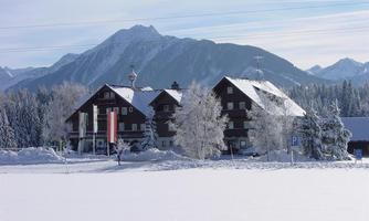A large building in winter with a snow-covered ground and snow-covered trees. Mountains can be seen in the background.