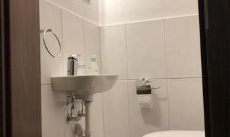A modern guest toilet with bright tiles and a small sink. The toilet is clean and well-lit.