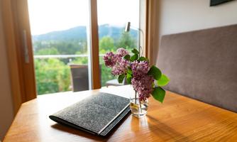 A cozy table with a notebook and a vase with purple flowers. In the background, there is a beautiful view of the landscape.