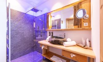 A modern bathroom with a glass shower and a wooden vanity. Stacked towels and a round mirror complement the stylish design.