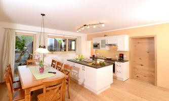 A bright and modern kitchen with a large wooden dining table. The windows provide plenty of daylight and a welcoming atmosphere.