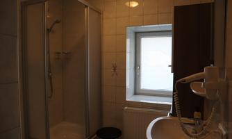A bathroom with a shower cubicle and a sink. The window provides natural light in the room.