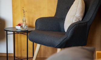 A cozy armchair with a cushion is situated next to a small table. On the table, there is a glass and a decorative flower.