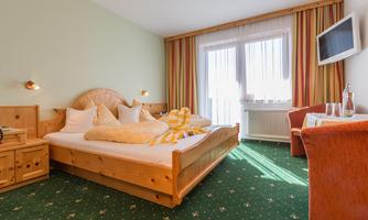 A cozy bedroom with a large bed and bright cushions. The room has windows with plenty of natural light and pleasant decoration.