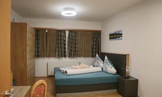 A simple room with a double bed and wooden furniture. The walls are neutral, and there are curtains as well as a modern lighting design.