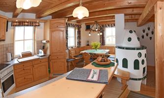 A cozy, rustic kitchen with wood paneling and a dining area. The fireplace and the large windows create a bright, inviting atmosphere.