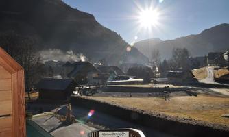 A peaceful mountain landscape with a clear blue sky and shining sun. In the foreground, there are some buildings and a playground.