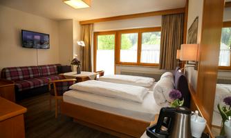 A cozy room with a double bed and a relaxation area. Large windows provide plenty of natural light and a pleasant atmosphere.