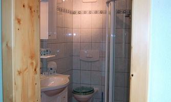 A bathroom with a modern shower, a sink, and a toilet. The walls are lined with tiles, and the room is well-lit.