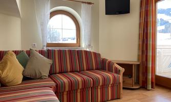 A cozy living room with a striped sofa and colorful pillows. Through the window, there is a beautiful view of the mountains.