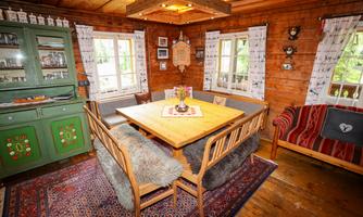 A cozy wooden room with a large dining table and comfortable seating. Decorative elements and photos hang on the walls.