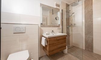 A modern bathroom with a glass shower and a wooden sink. The walls are designed in light colors, and a mirror reflects the room.