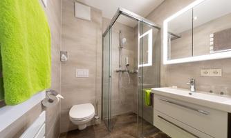 A modern bathroom with a shower, sink, and toilet. Green towels provide a splash of color in the elegant design.