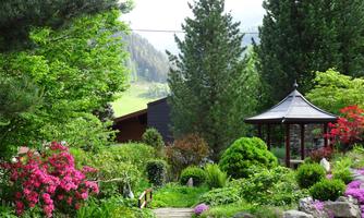 A beautiful garden with colorful flowers and green shrubs. In the background, there is a pavilion and trees surround the landscape.