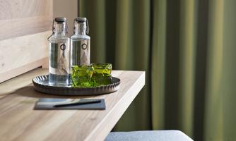 A stylish table with two water bottles and a green glass on a tray. In the background, green curtains can be seen.