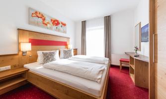 A bright and modern bedroom with two beds. The room is cozily furnished and has large windows with curtains.