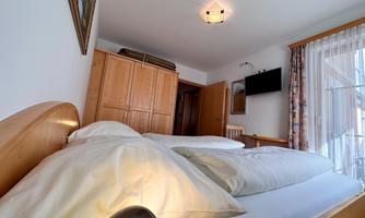 A cozy bedroom with a large bed and soft pillows. There is a wardrobe and a window with curtains.