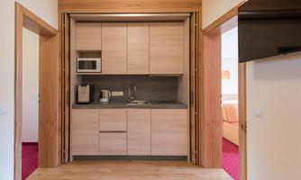 A modern kitchen unit with wooden cabinets and a gray workspace. It is equipped with a kettle and a microwave.