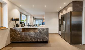 Modern kitchen with an elegant kitchen island and high-quality appliances. Ample daylight from large windows creates an inviting atmosphere.