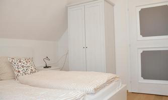A cozy bedroom with a double bed and a bright bedspread. In the background, there is a white wardrobe and an attractively designed door.