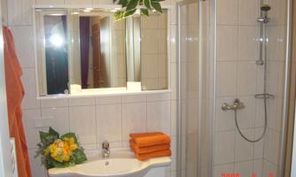 A modern bathroom with a shower and a sink. Orange towels and plants give the space a friendly atmosphere.