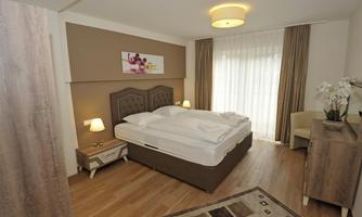 A bright bedroom with a double bed, a beautiful rug, and modern wooden furniture. Large windows let in plenty of light and create an inviting atmosphere.