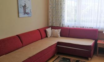 A cozy living room with a red couch and a beautiful carpet. Large windows let in plenty of light and the curtains are color-coordinated.