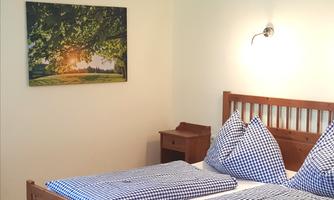 A cozy bedroom with wooden furniture and checkered bedding. On the wall hangs a beautiful picture of a sunny landscape.